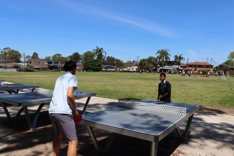 Students playing table tennis in the foreground whilst a group of students play soccer in the background.